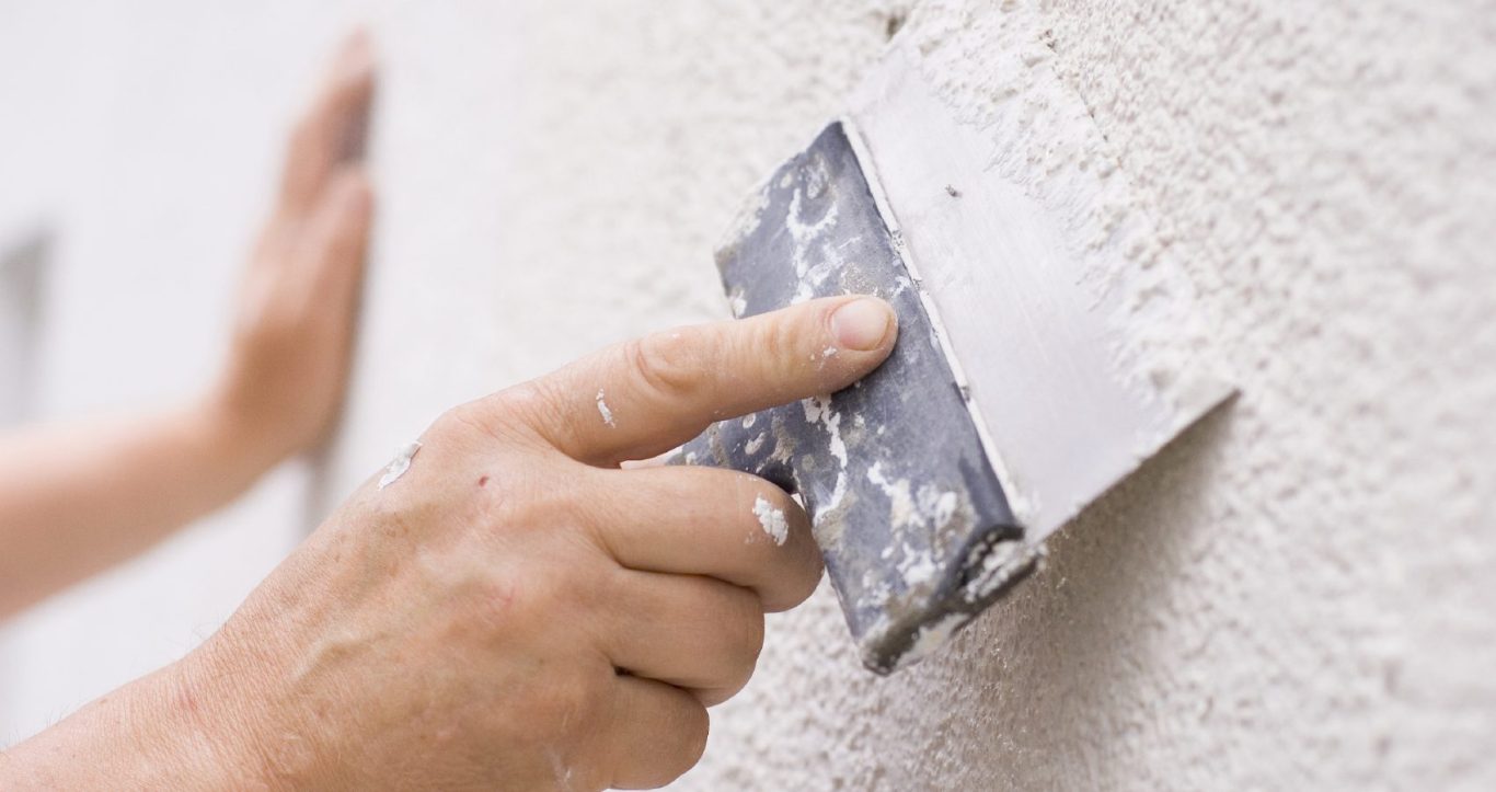 Hand using a trowel to apply render to an exterior wall.